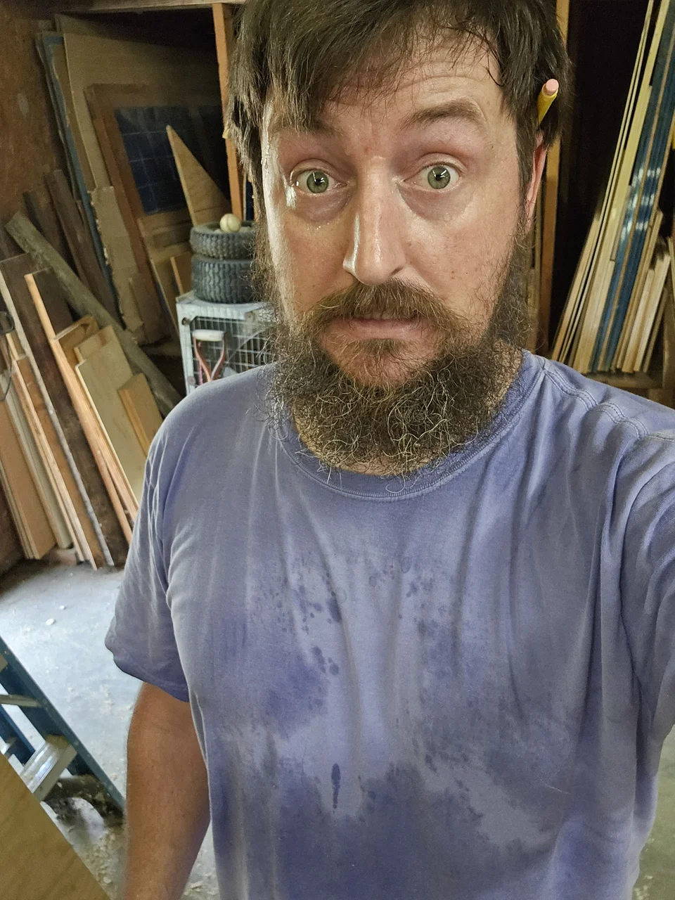 Kendal Hern in the shop, in a work shirt, with lumber racked behind him.