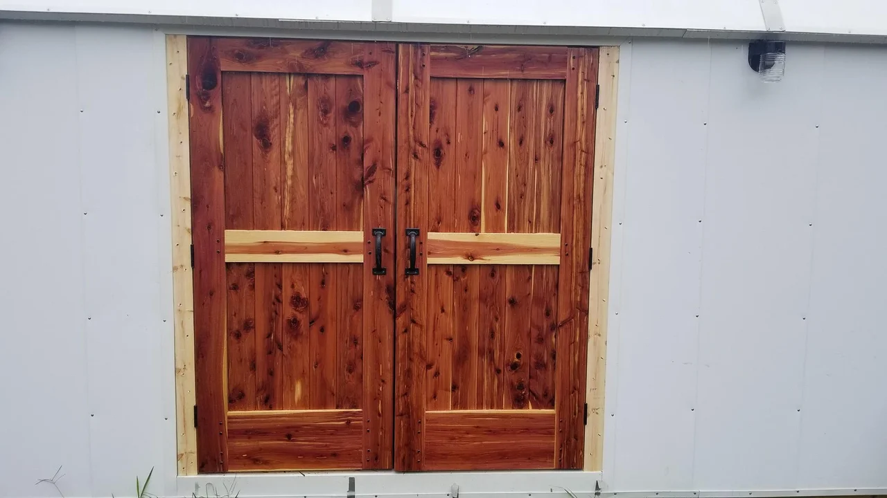 Finished cedar double doors installed in a white wall.