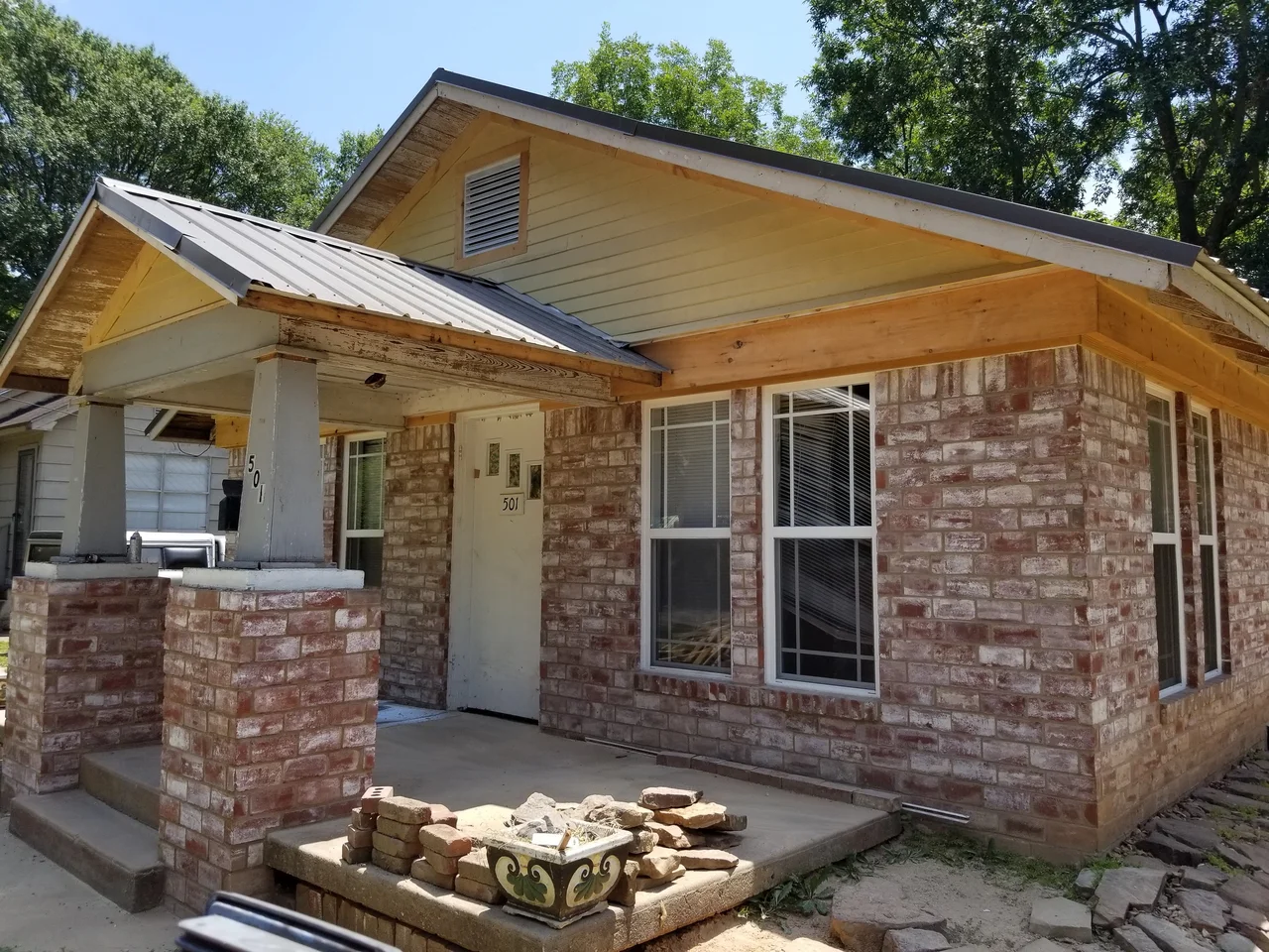 A brick house with a new standing-seam porch roof carried on cedar posts and beams.