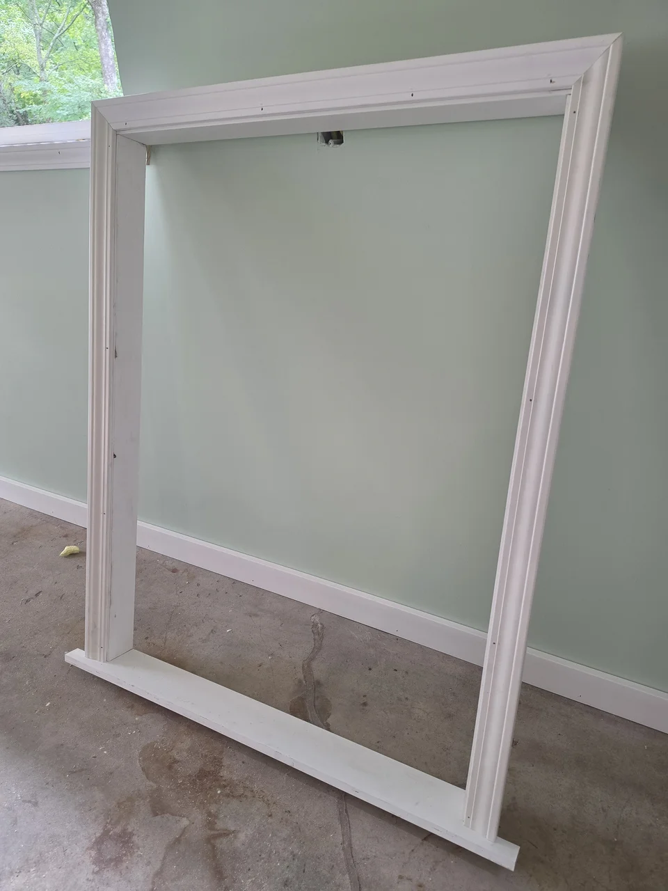 A white door and window casing assembly leaning against a finished green wall.