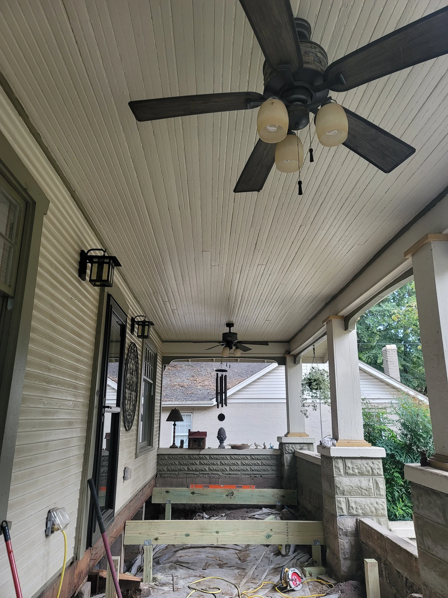 A Craftsman porch with beadboard ceiling, ceiling fans, sconces and tapered columns on stone piers.