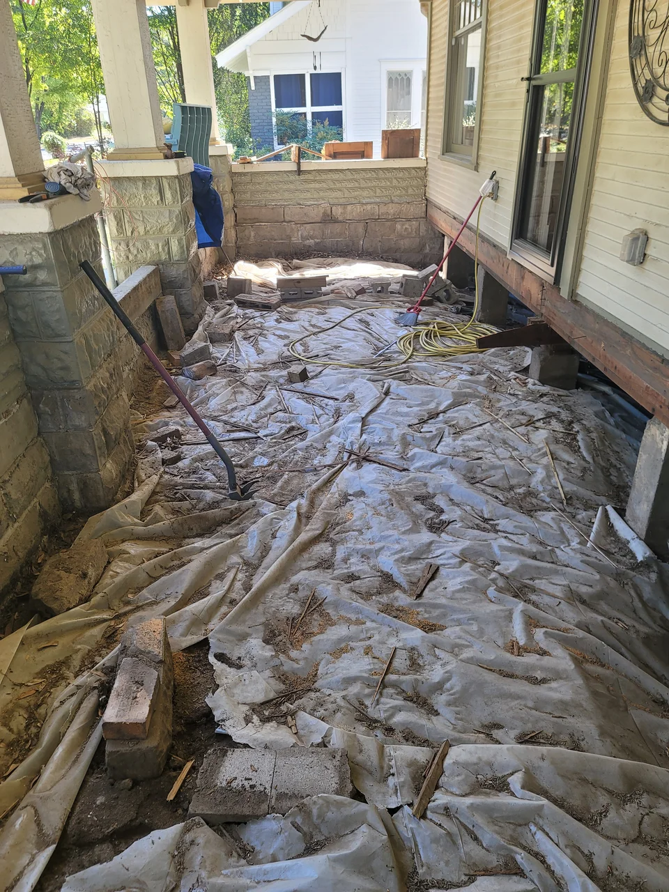 The front porch torn out to bare dirt under plastic sheeting.