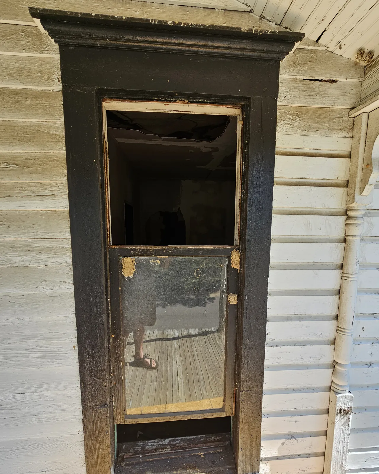A Latimore window opening before restoration: empty frame, failed trim, peeling siding.