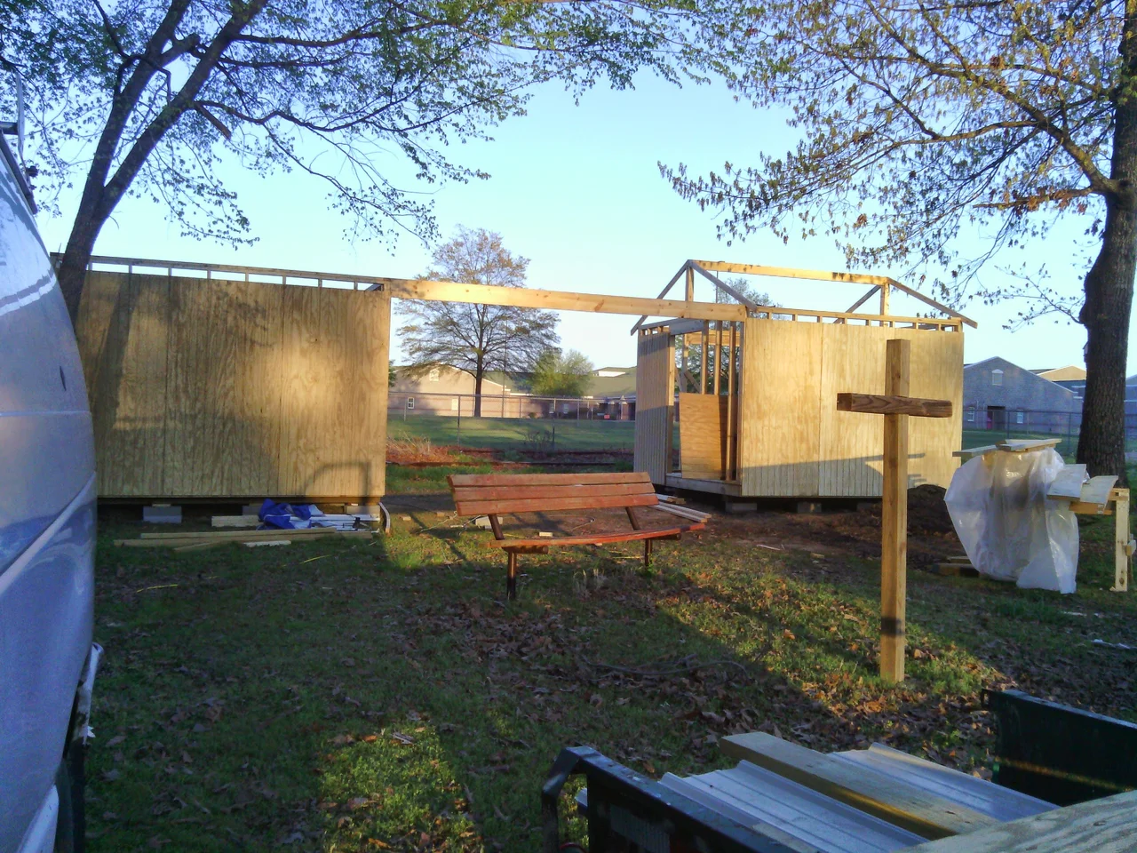 The shed frame standing in the community garden with the church cross beyond.