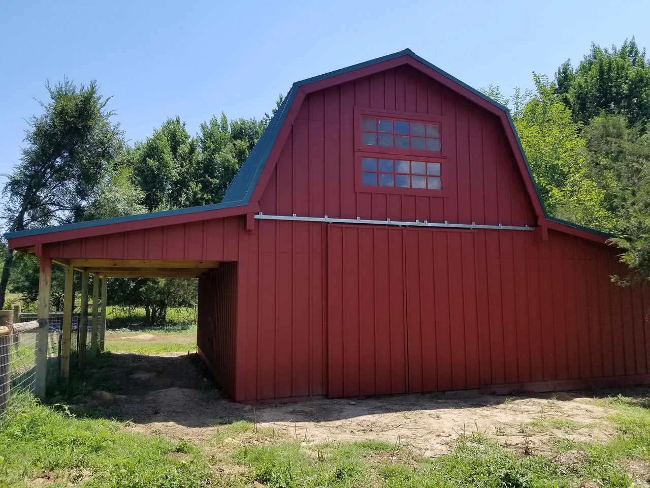 The finished red gambrel barn with loft window and green metal roof.