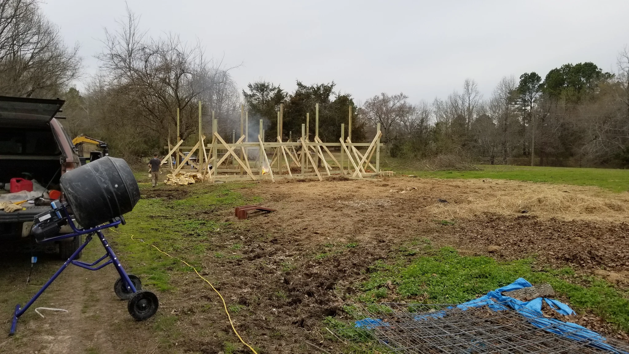 The early framing skeleton of a barn standing in an open field.