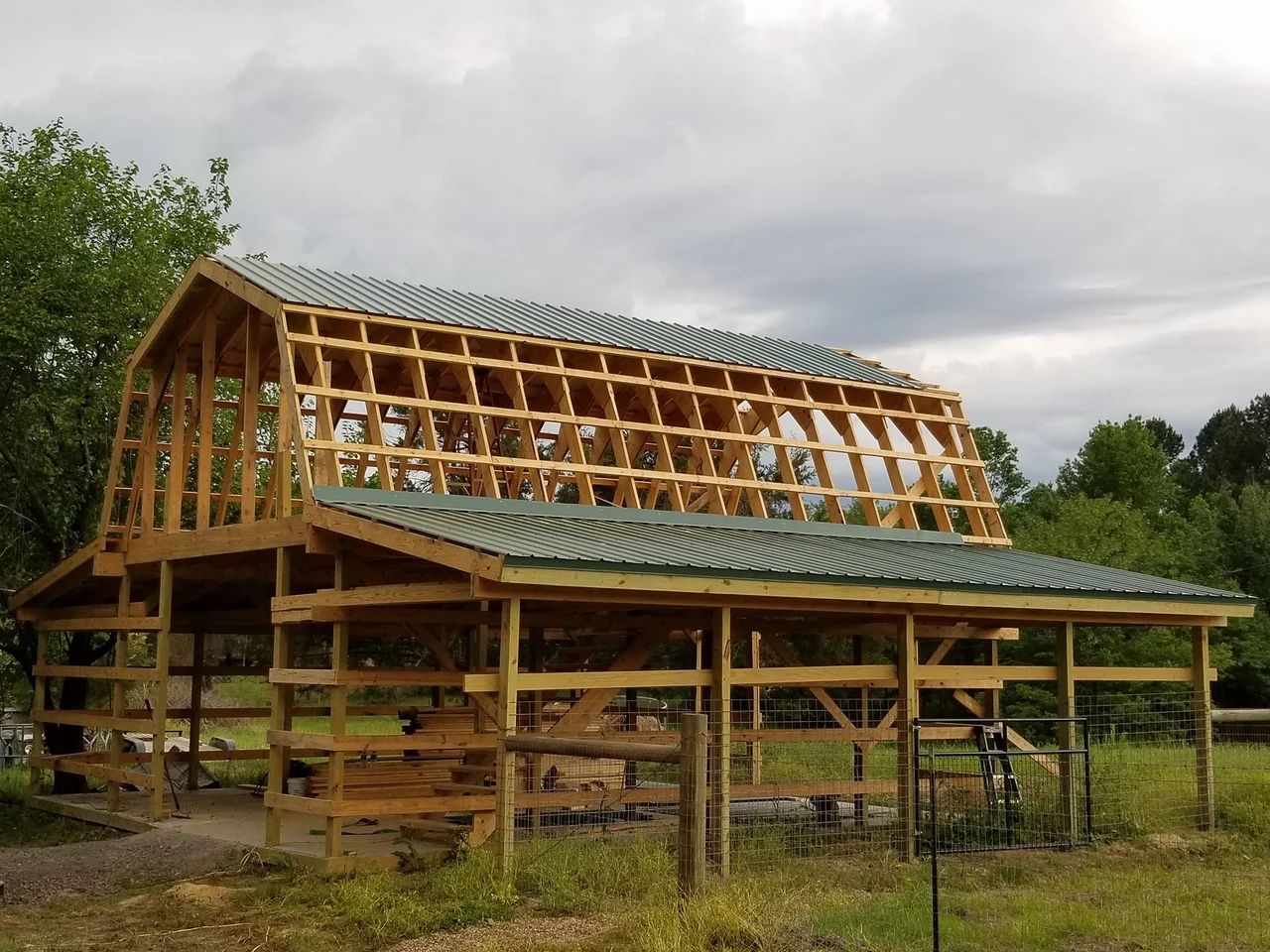 Green metal roofing being installed over the barn's truss framing.