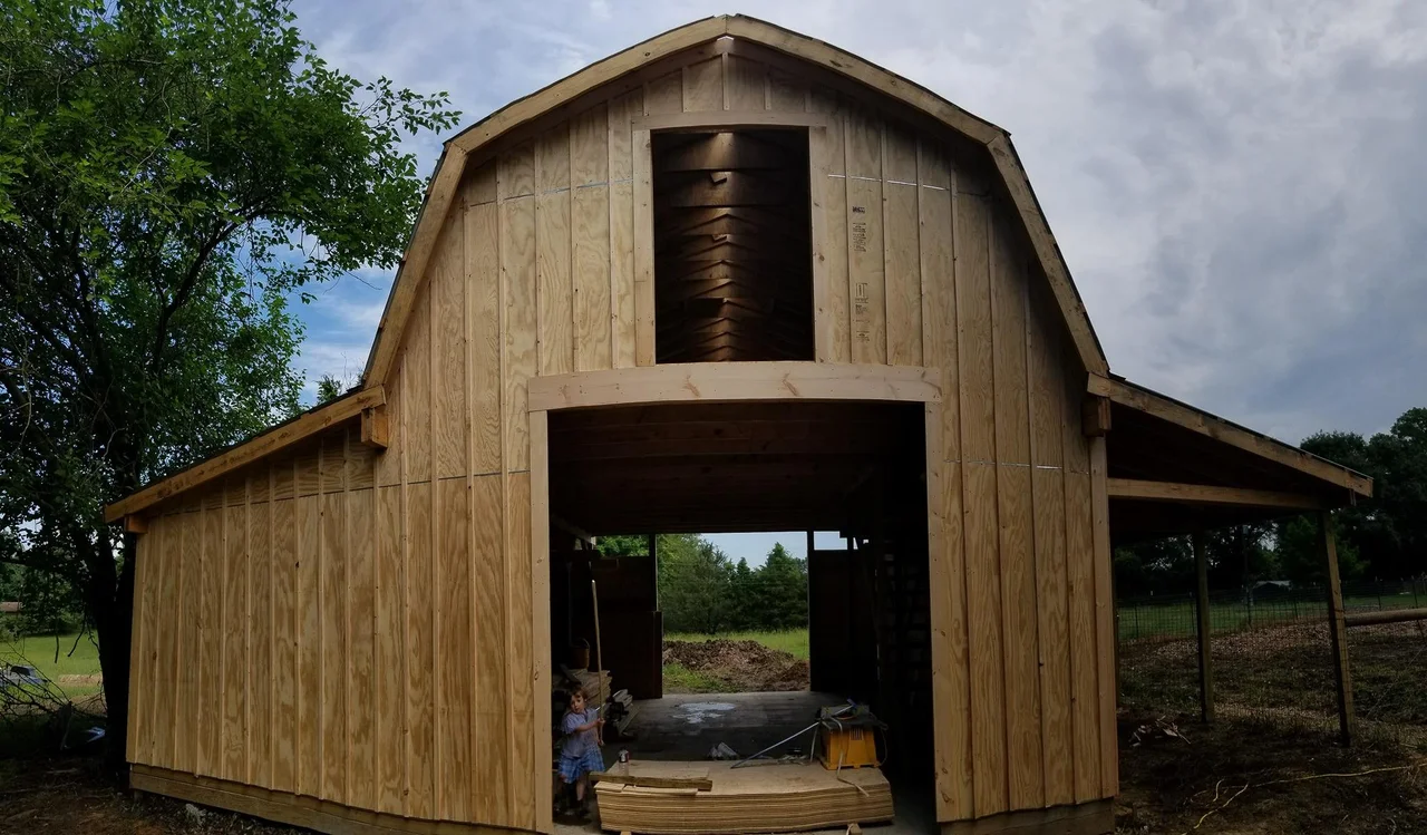 The barn clad in unpainted board-and-batten siding with a large central opening.