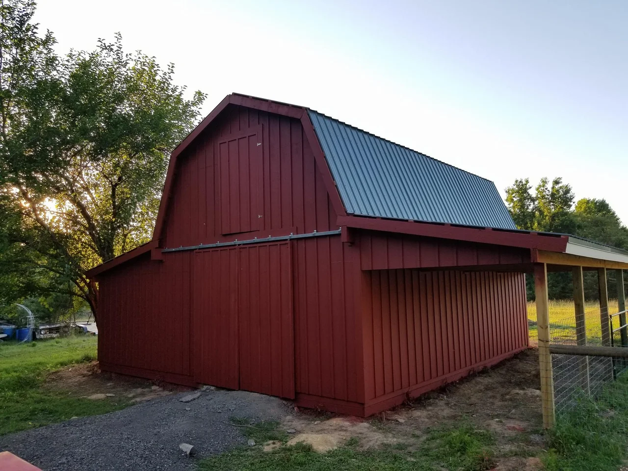 The finished red barn in warm low-angle light, metal roof catching the sun.