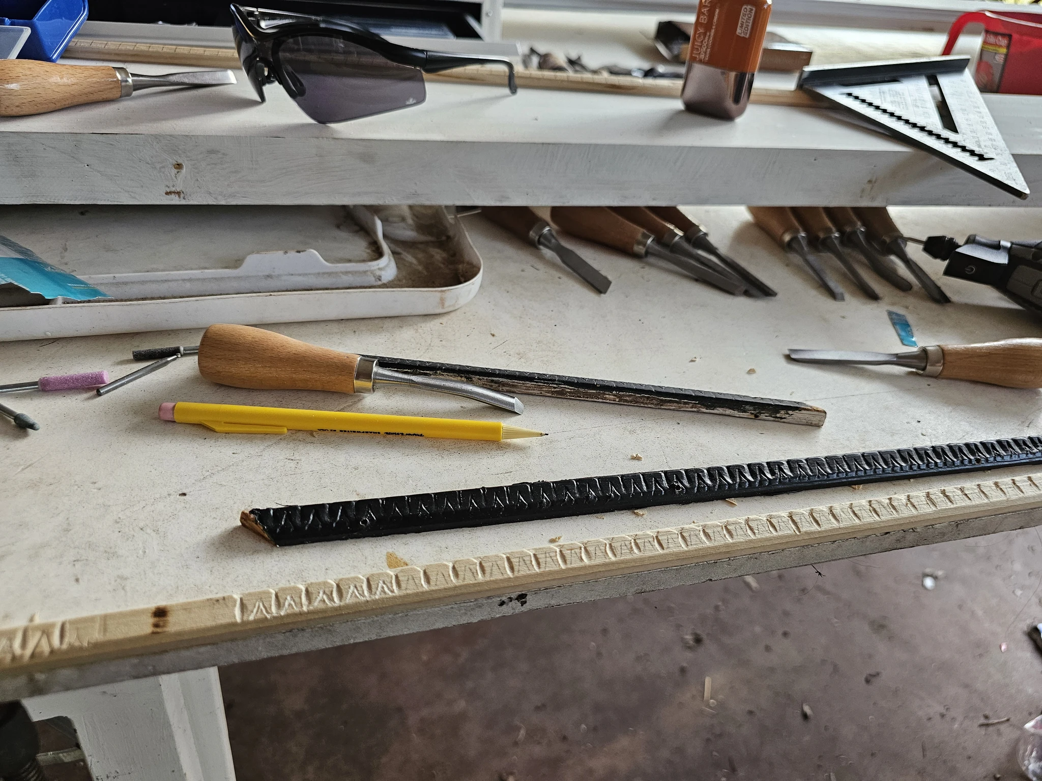 Carving in progress on a moulding profile, with gouges and a pencil for scale.
