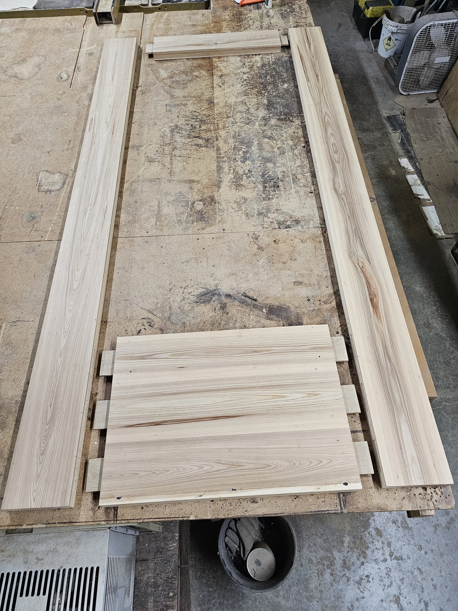 Door stiles, rails and panels milled from pale hardwood and laid out on the shop floor.