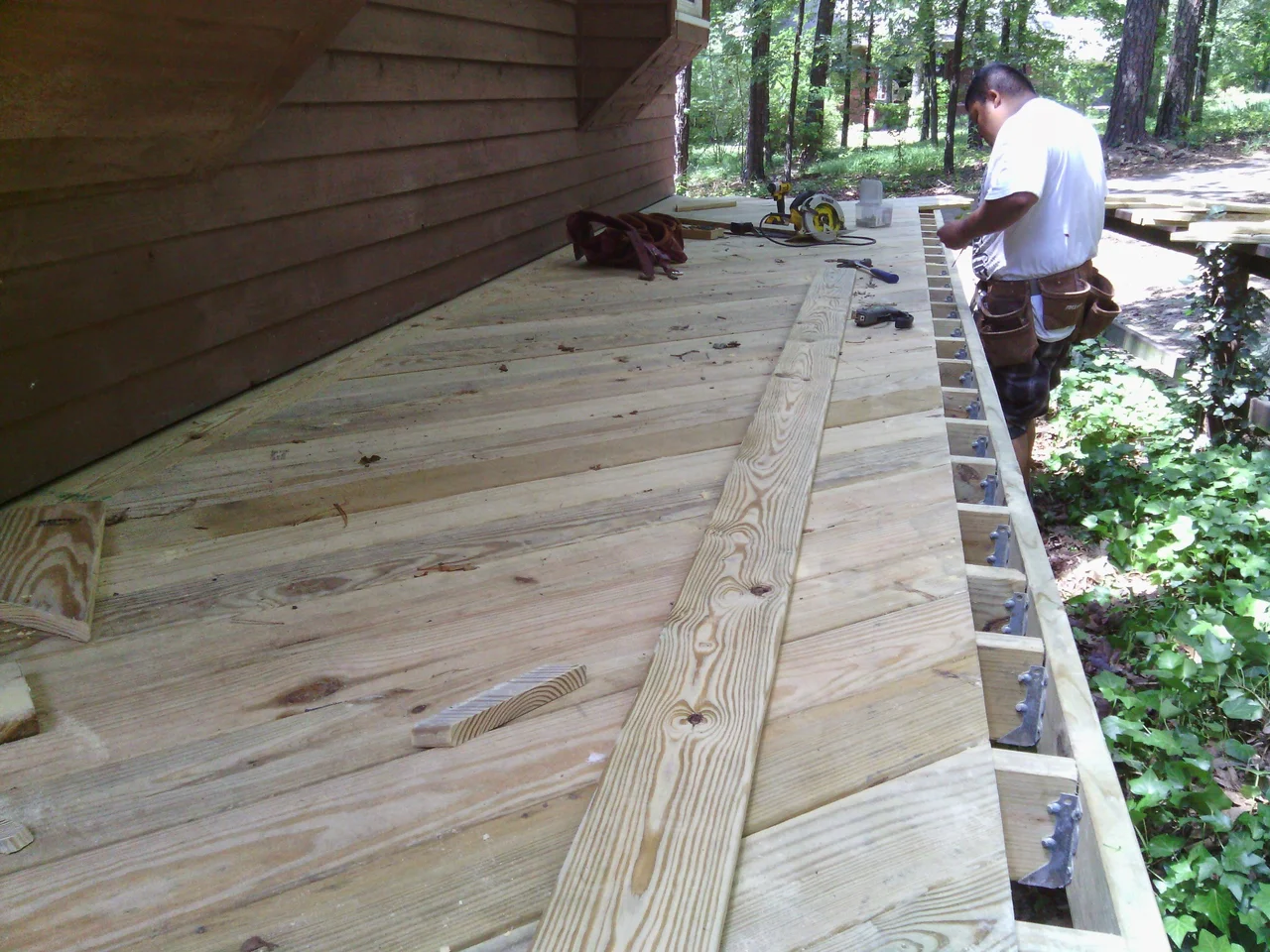 A carpenter setting a border board with joists still open alongside.