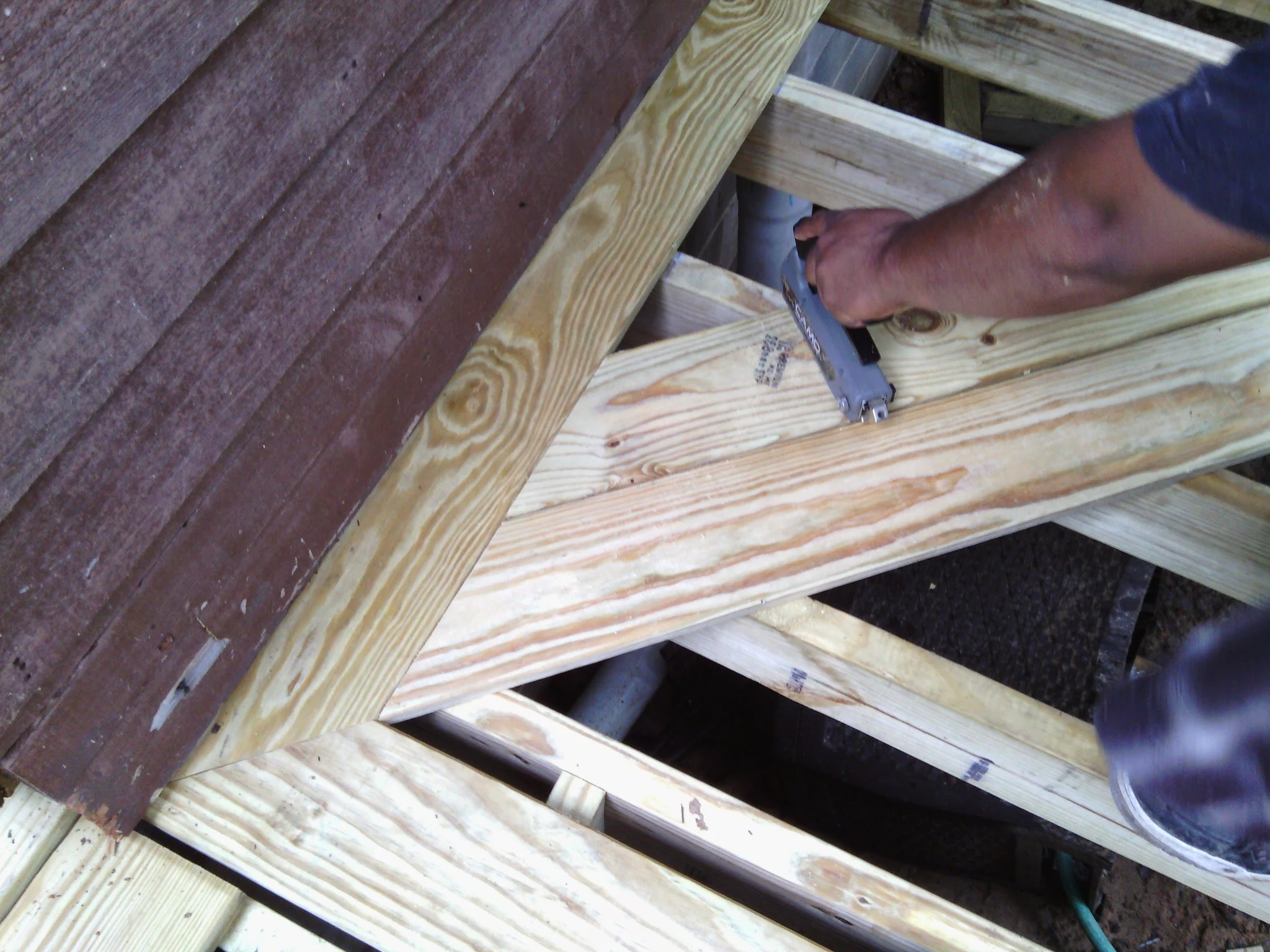 Close view of a joist-to-ledger connection being fastened by hand.