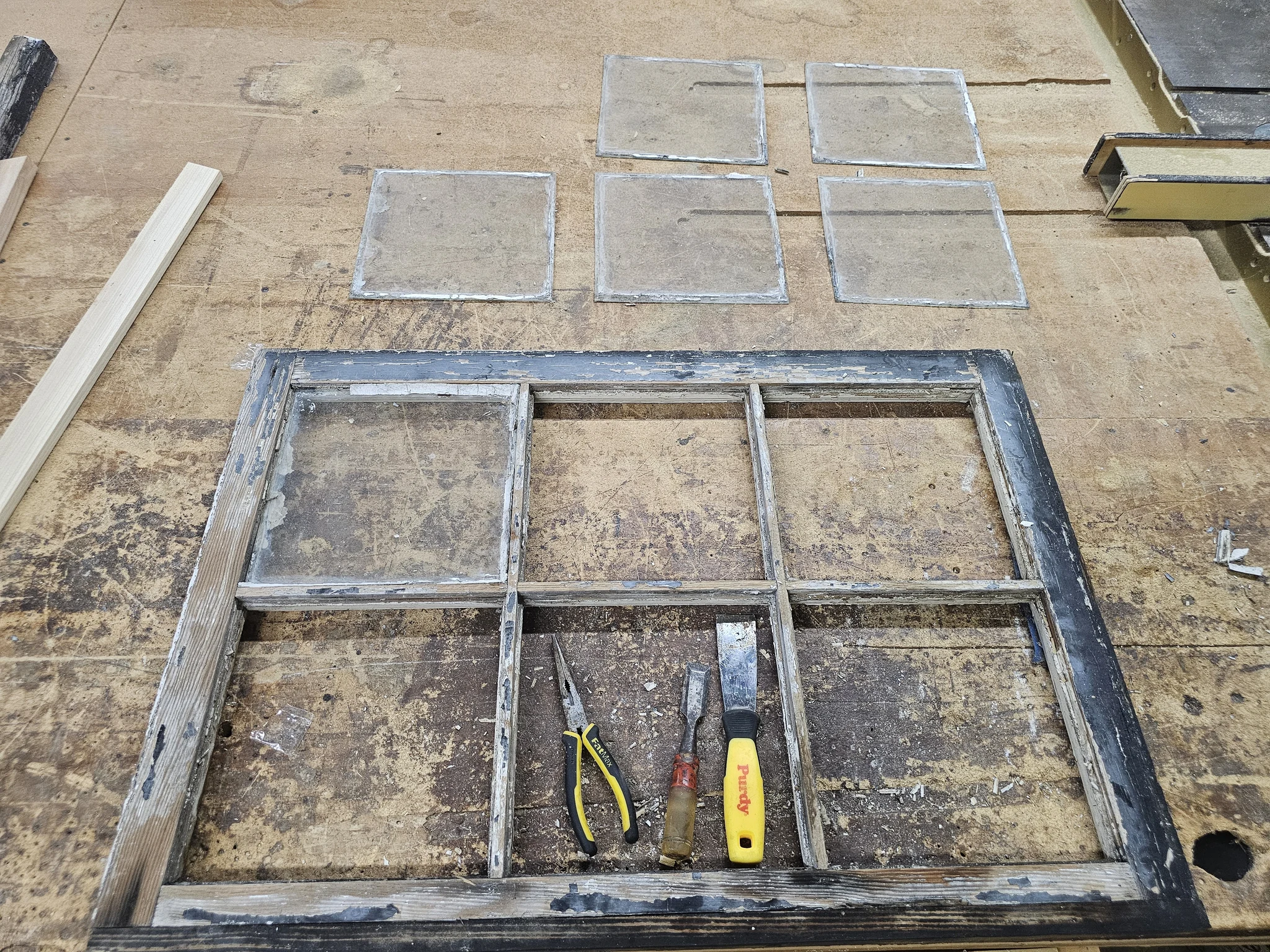 An original six-light sash stripped bare with its wavy glass and hand tools laid out.