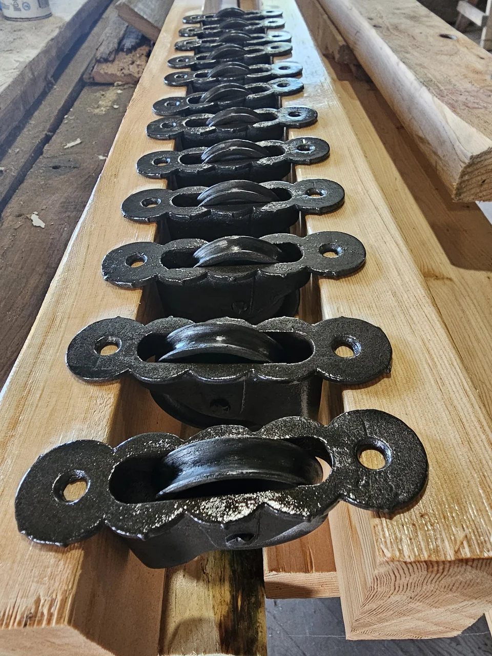 A row of restored cast-iron sash pulleys resting on freshly milled stock.