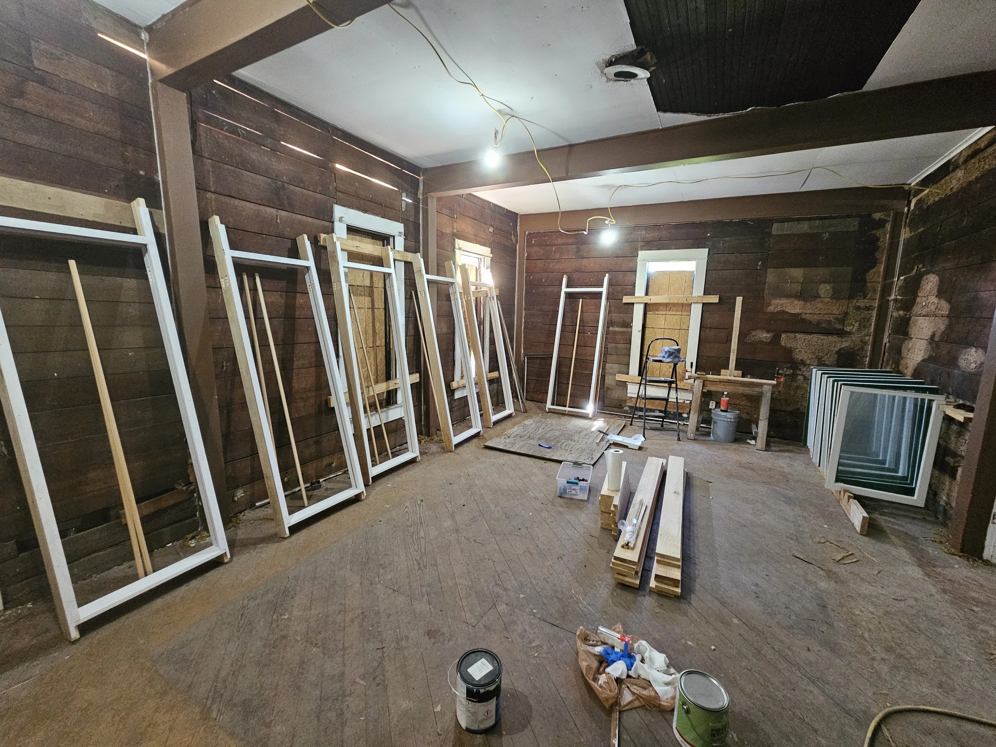 The interior with original board walls and restored sash stacked around the room.