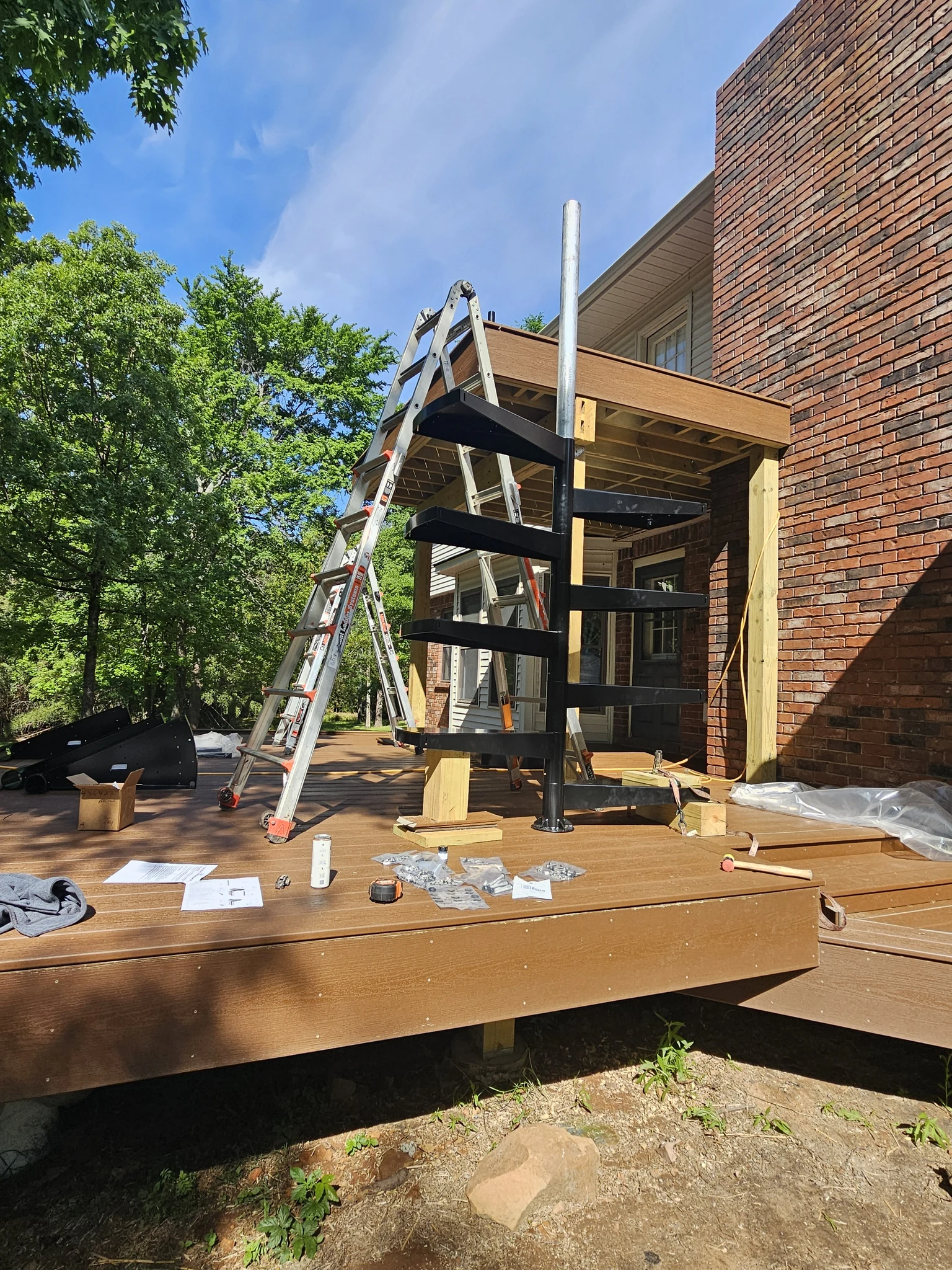 The spiral stair centre column standing on the deck with its lowest treads fitted and a ladder alongside.
