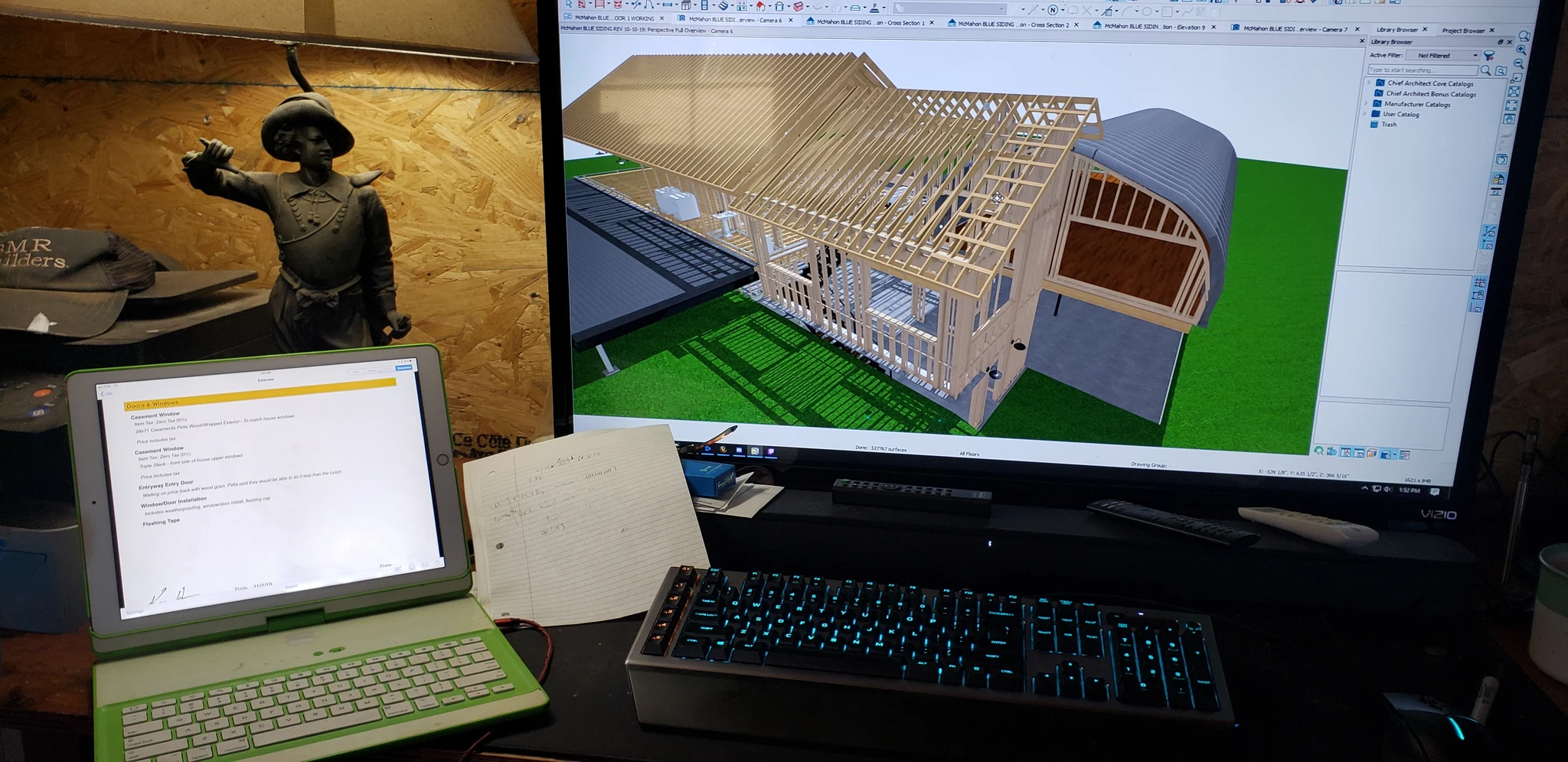 A desktop monitor showing a SketchUp model of the house framing under construction.