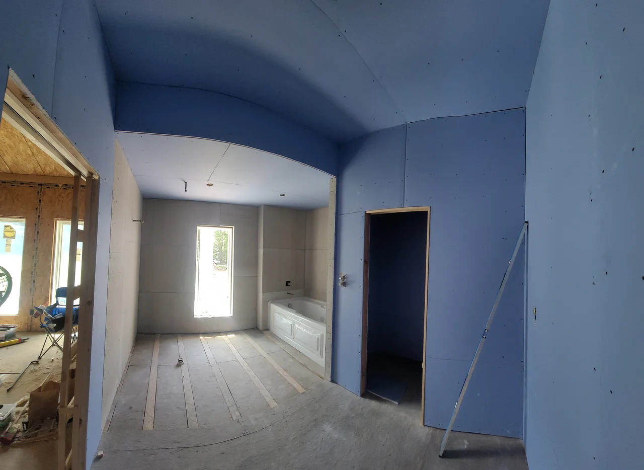 A room with a vaulted drywall ceiling and a window at the end.