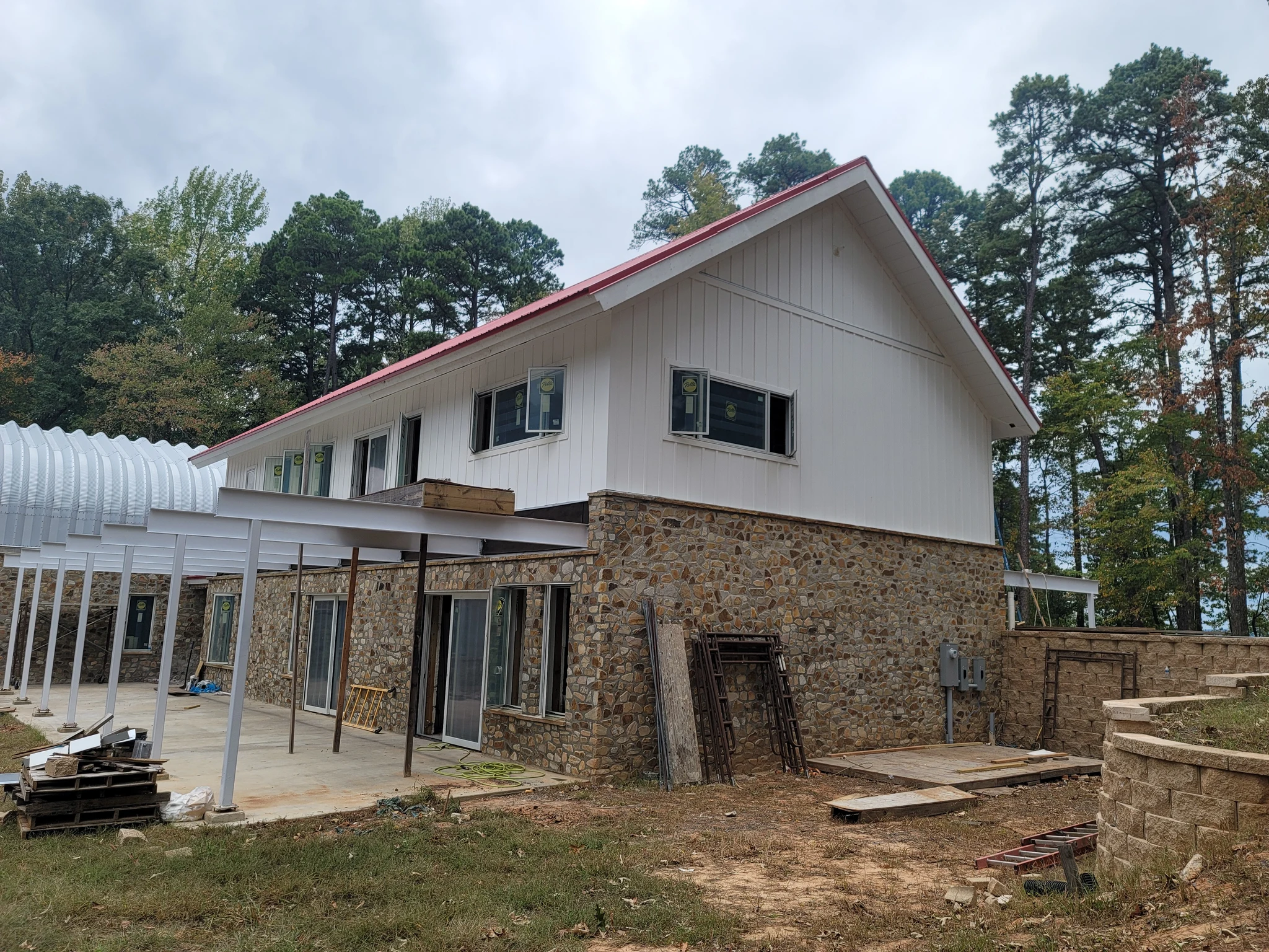 Full elevation of white siding and red roof over a stone base, with a covered walk.