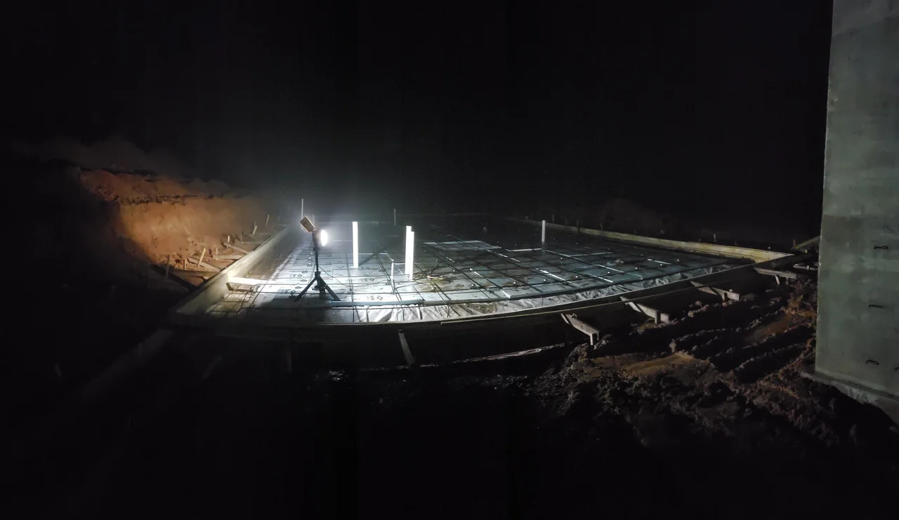 Concrete footing forms lit by a single work light after dark.