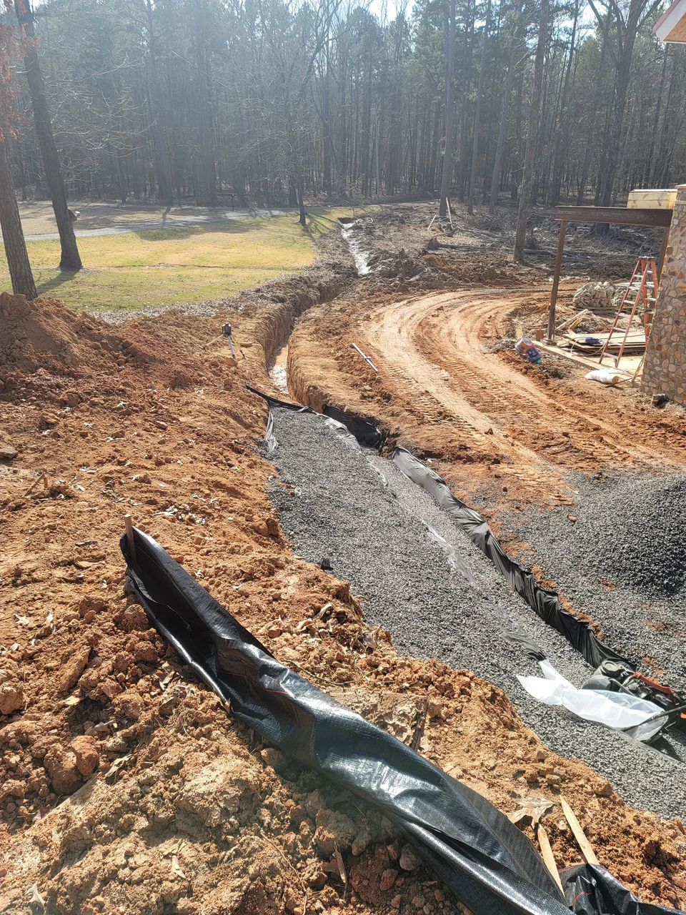 A drainage swale cut through red clay and lined with gravel, curving away from the building.