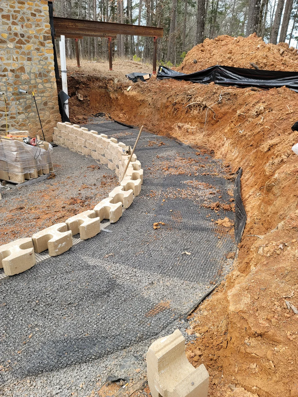 A curved retaining wall of segmental block holding back cut clay beside a gravel drive.