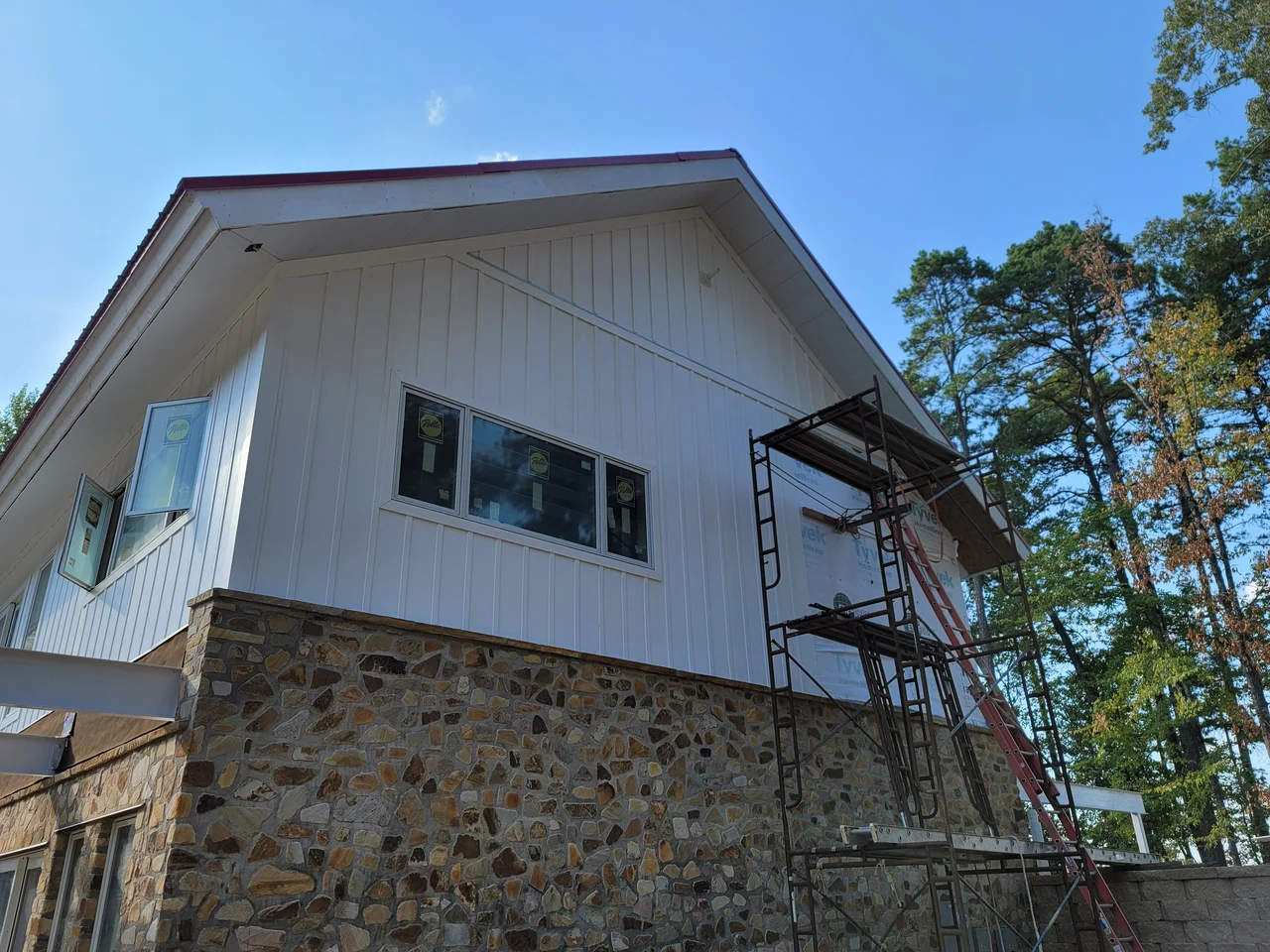 The white board-and-batten gable above the stone base, scaffolding still standing against it.