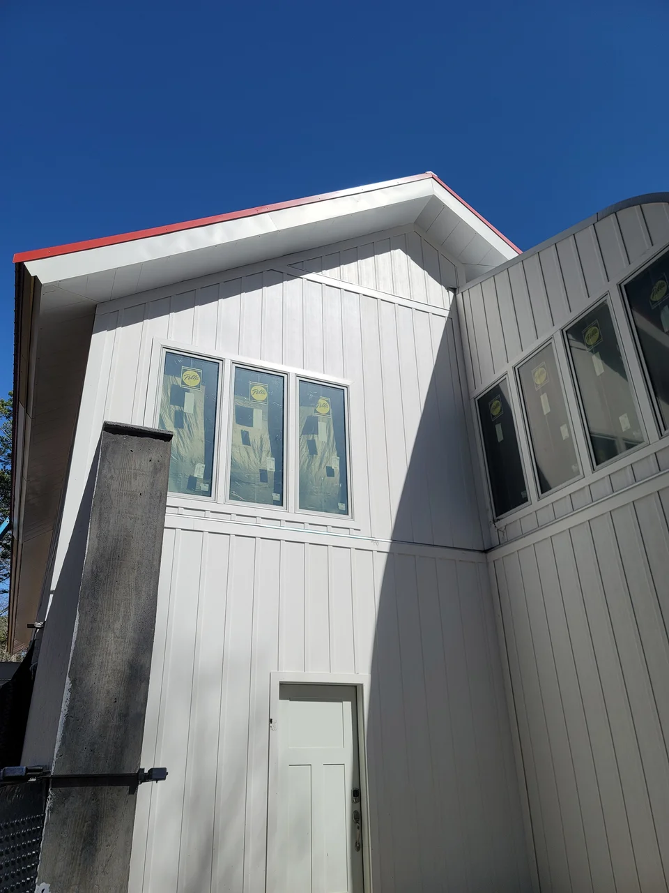 The upper walls in white siding where the two roof planes meet above a run of tall windows.