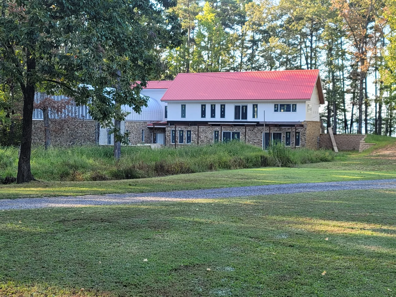 The house seen from across the lawn — stone lower storey, white upper, red roof among the pines.