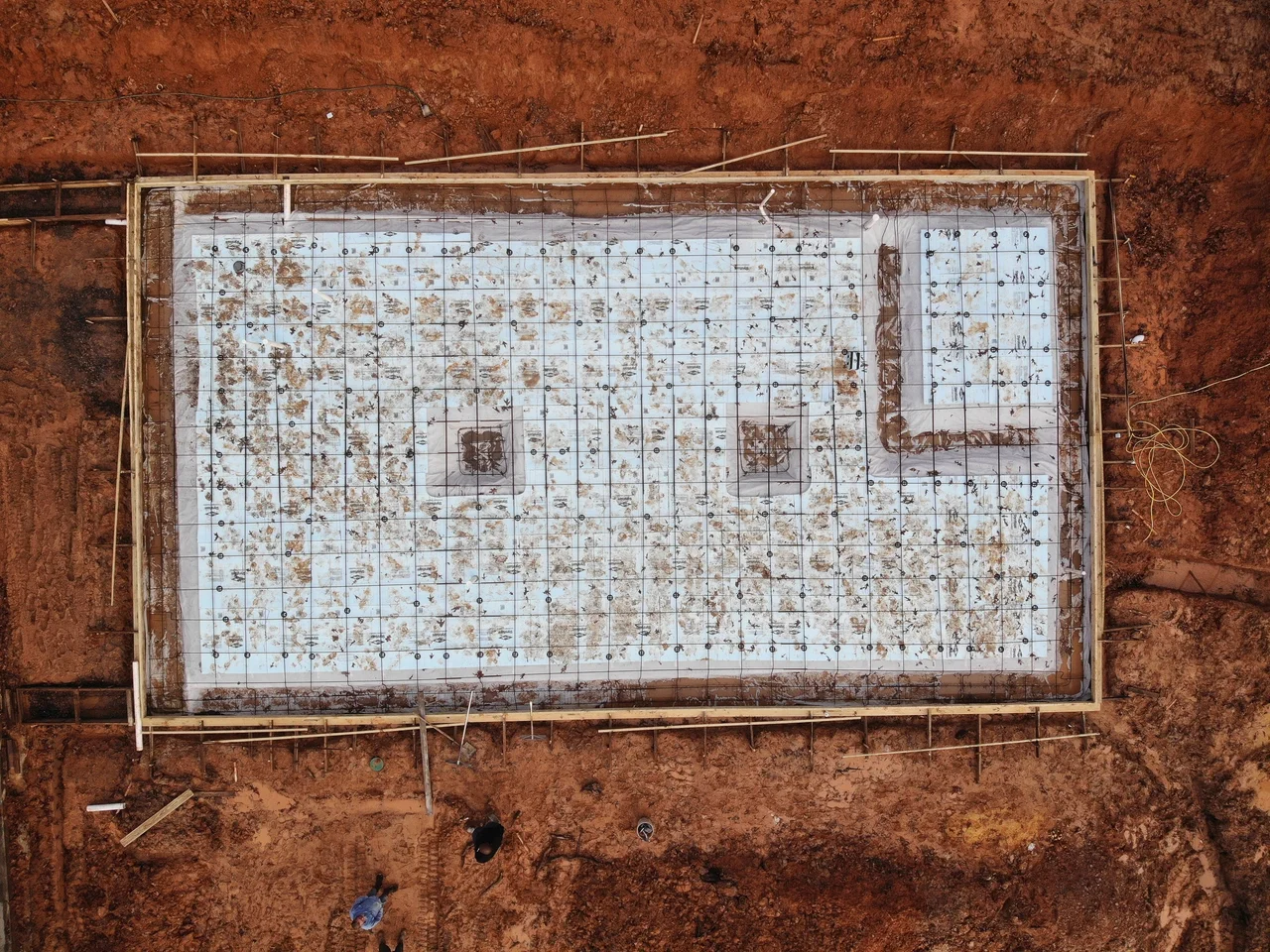 Aerial view of the prepared basement slab with vapour barrier, rebar mat and formed footings set into red clay.