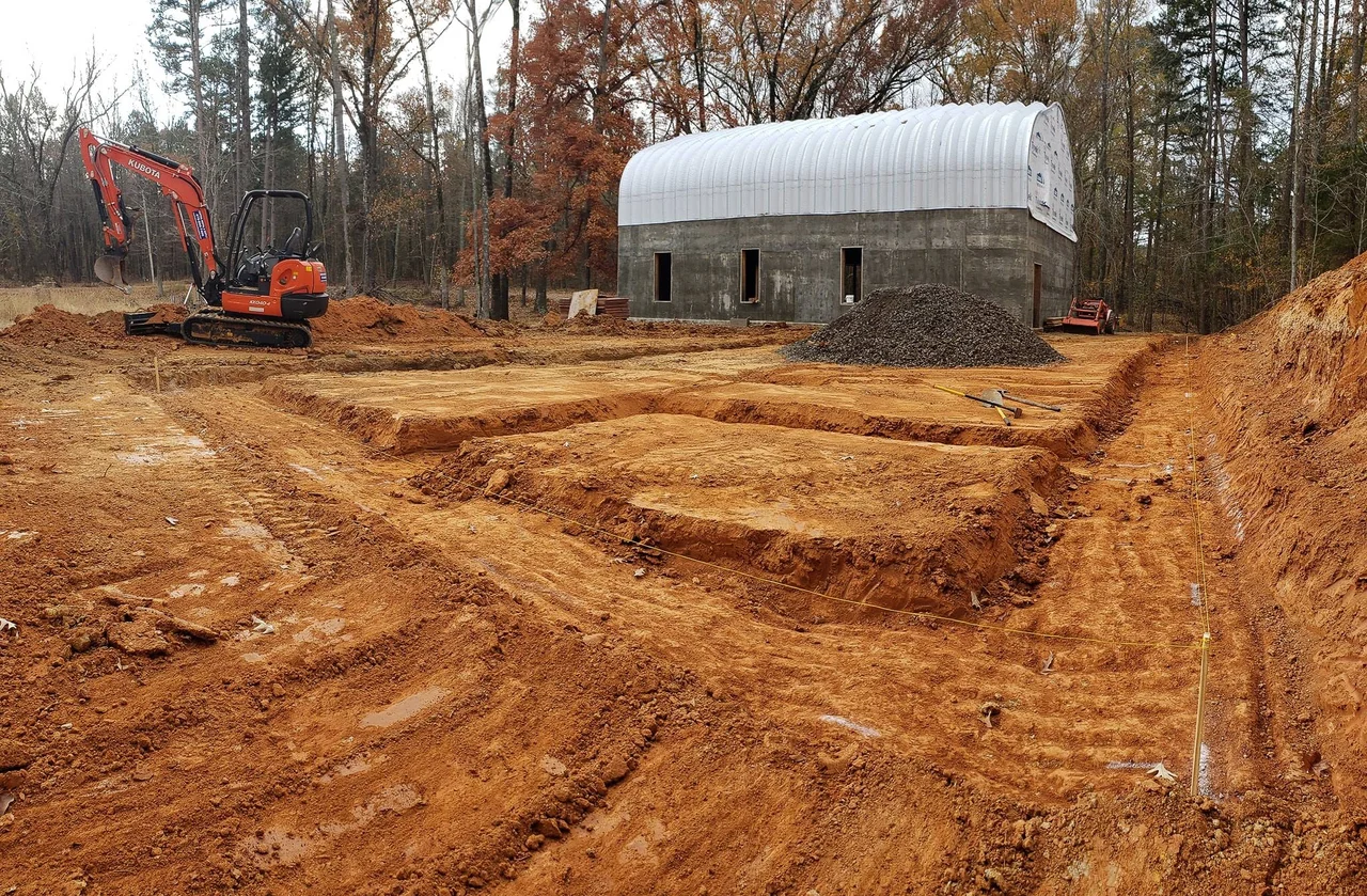 An excavator shaping grade beside the concrete structure.