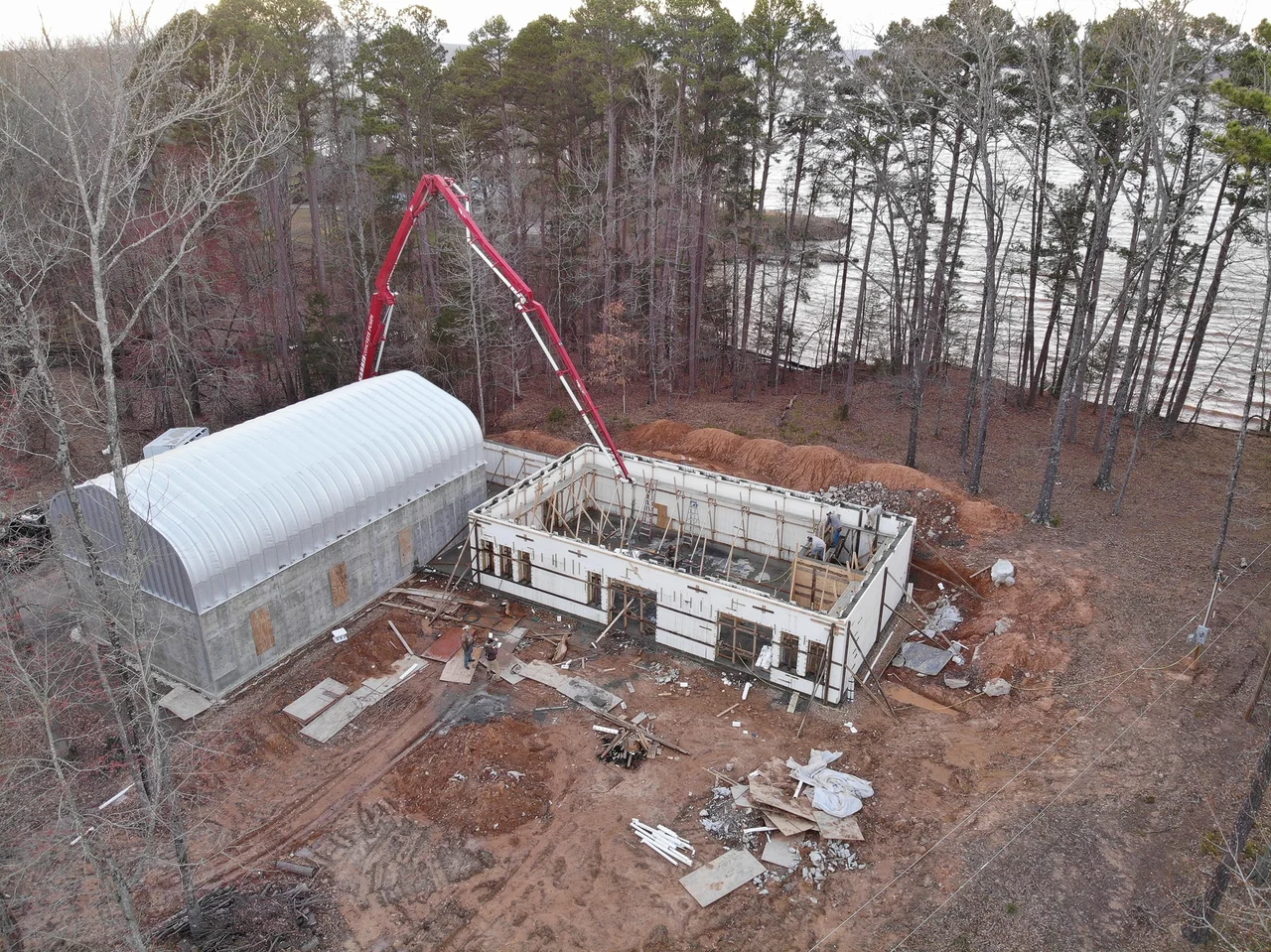 Aerial view of a concrete pump boom filling ICF walls beside the steel arch building.