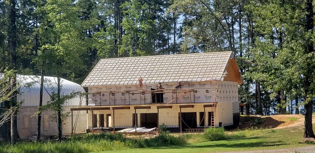 The upper framing sheathed and roofed, arch building behind.