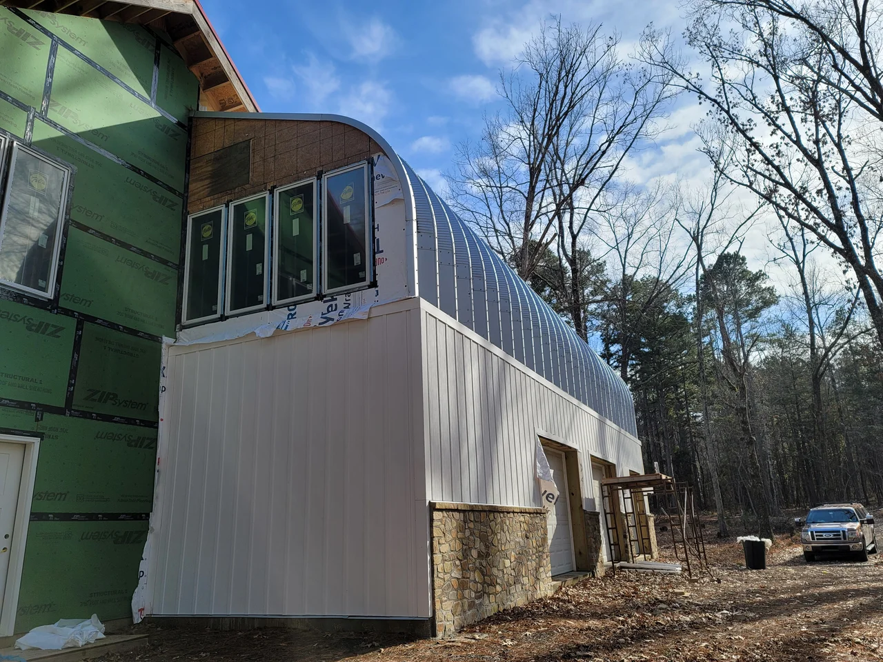 The white corrugated flank of the arch building with a green-sheathed gable beyond.