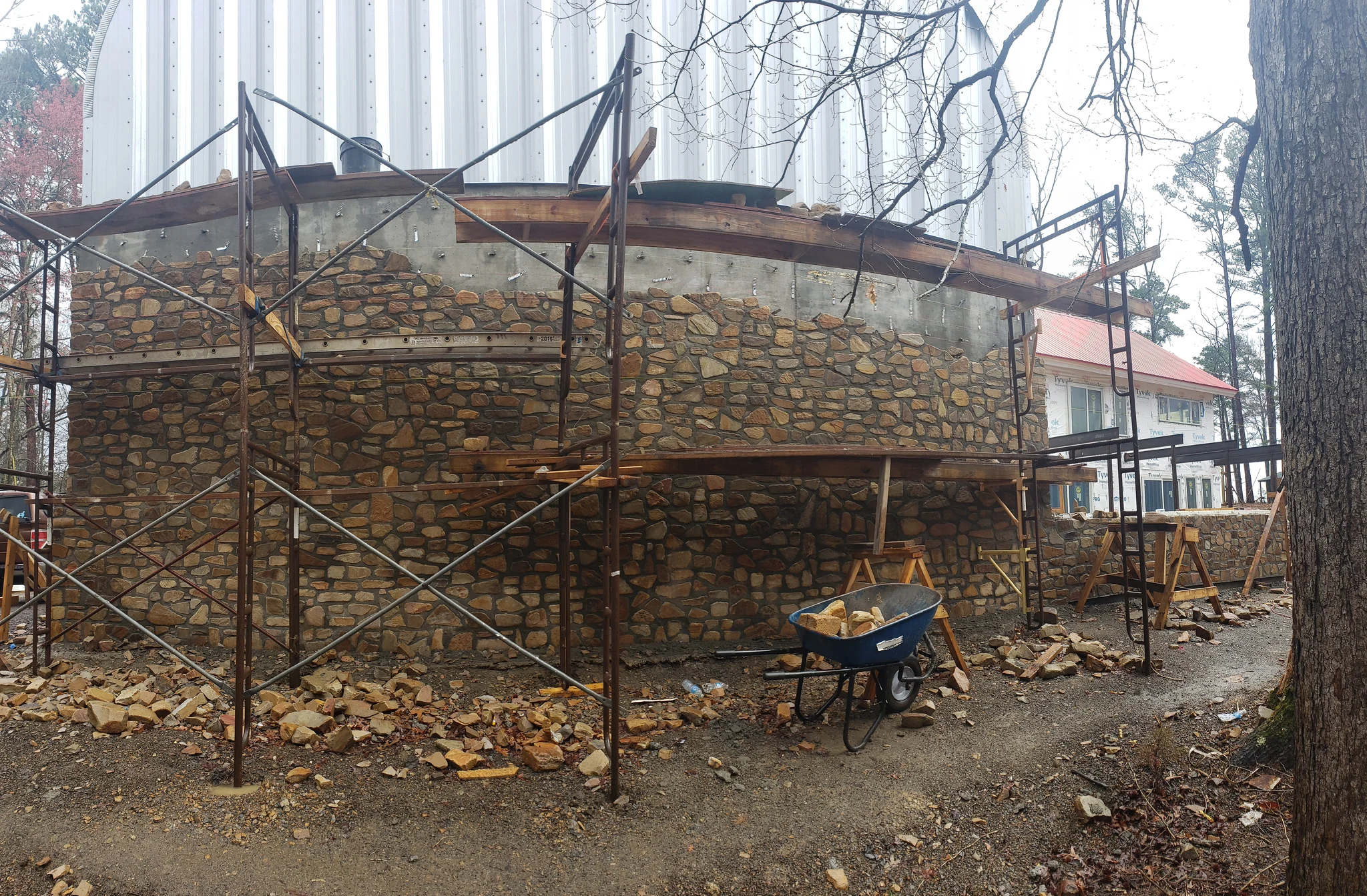 A curved stone wall under construction with scaffolding around it.