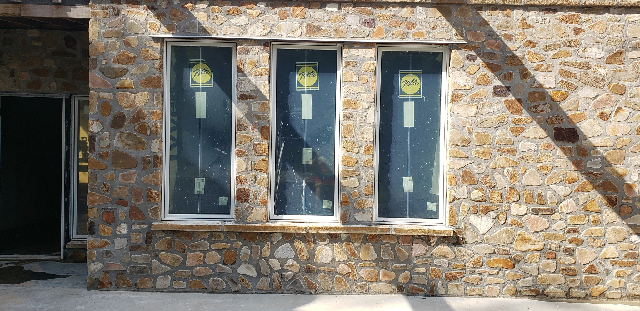 Finished stone facade with three tall windows set into it.
