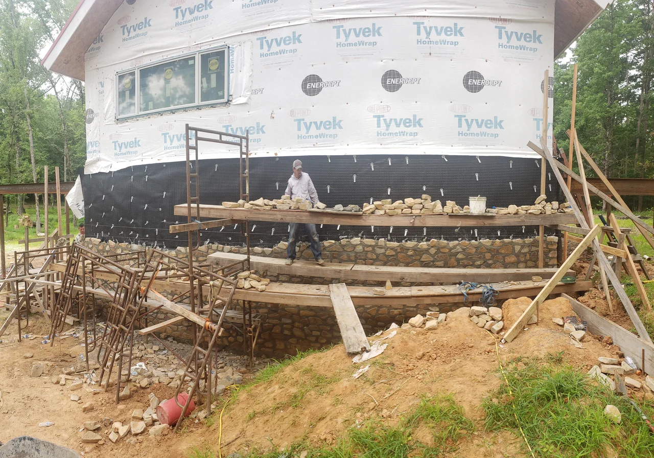 Wide view of the curved stone wall rising against the waterproofed structure.