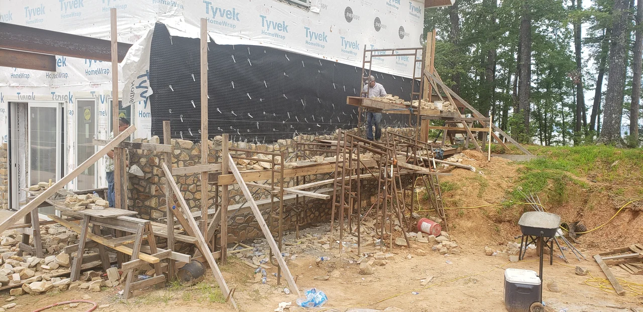 Stone facing rising against a black waterproofing membrane on scaffolding.