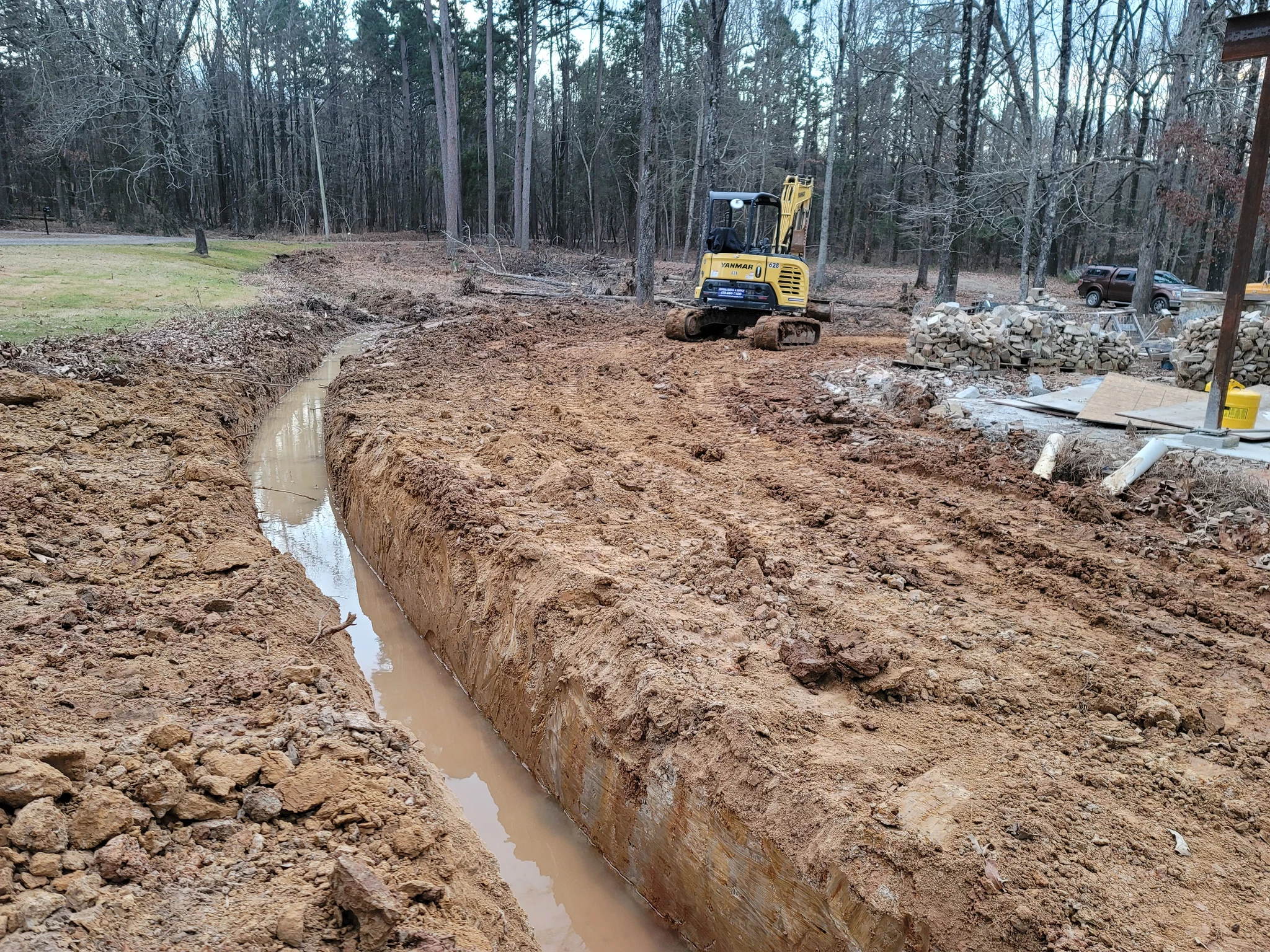 An excavator cutting a drainage trench in red clay.