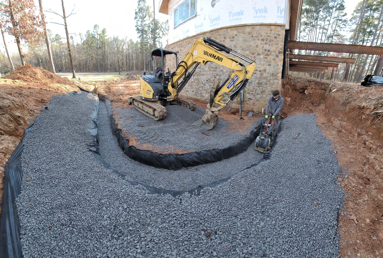 A curved drainage channel lined with fabric and filled with gravel.