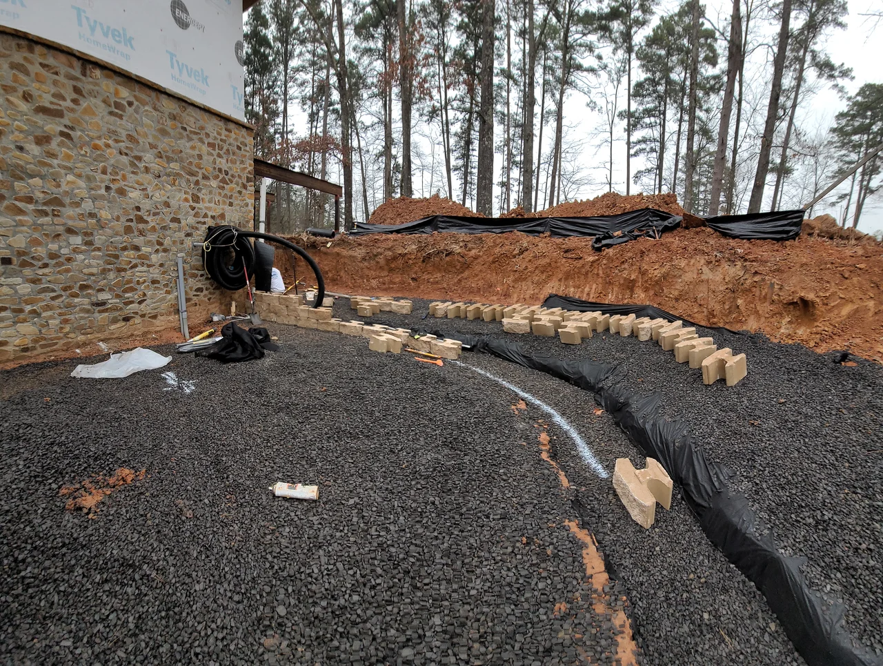 Conduit and drainage pipe run through a gravel bed beside the stone wall.