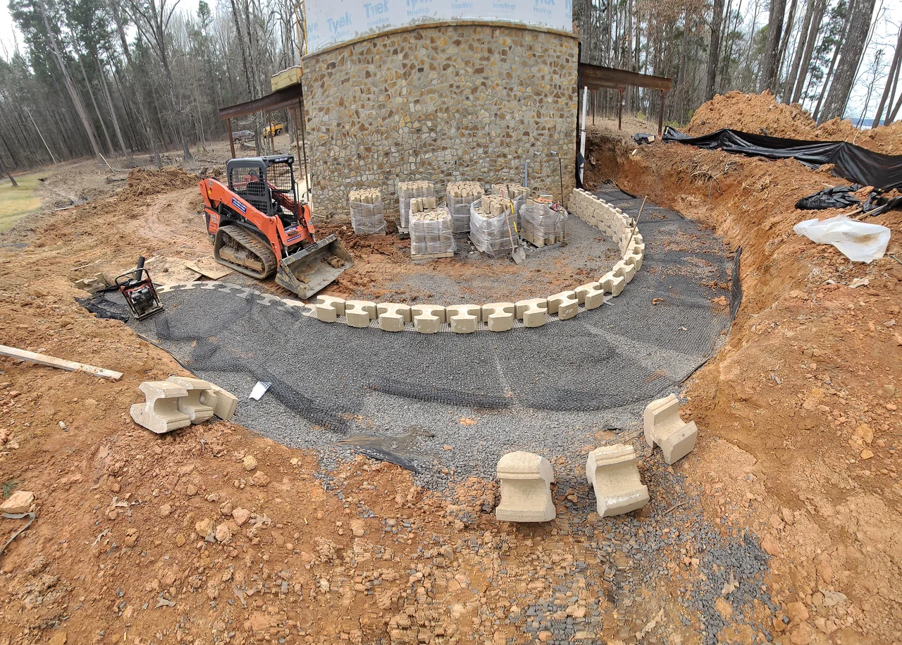 A skid steer working the curved gravel turnaround against the stone base.