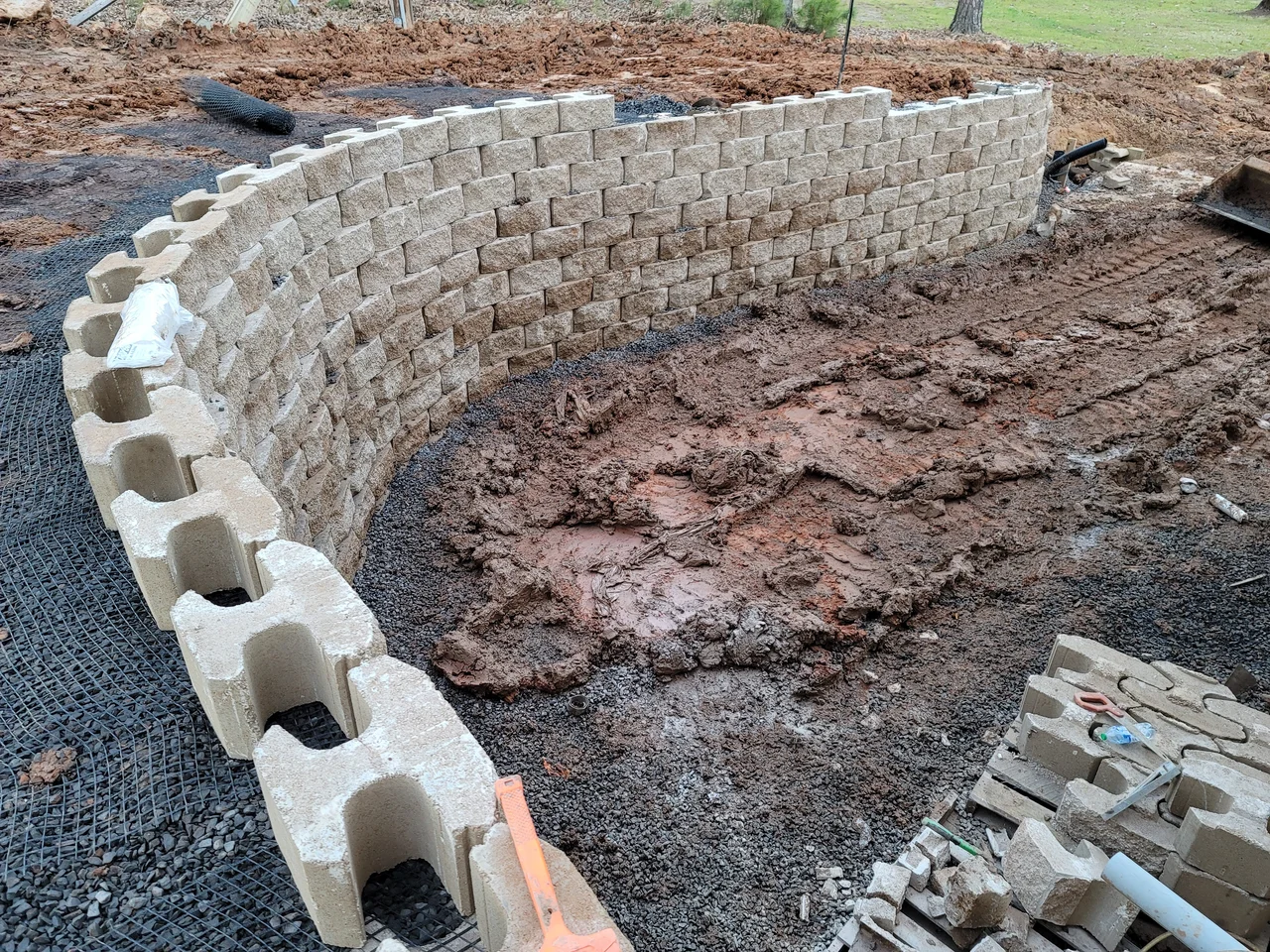 A curved segmental retaining wall under construction with drainage stone behind.