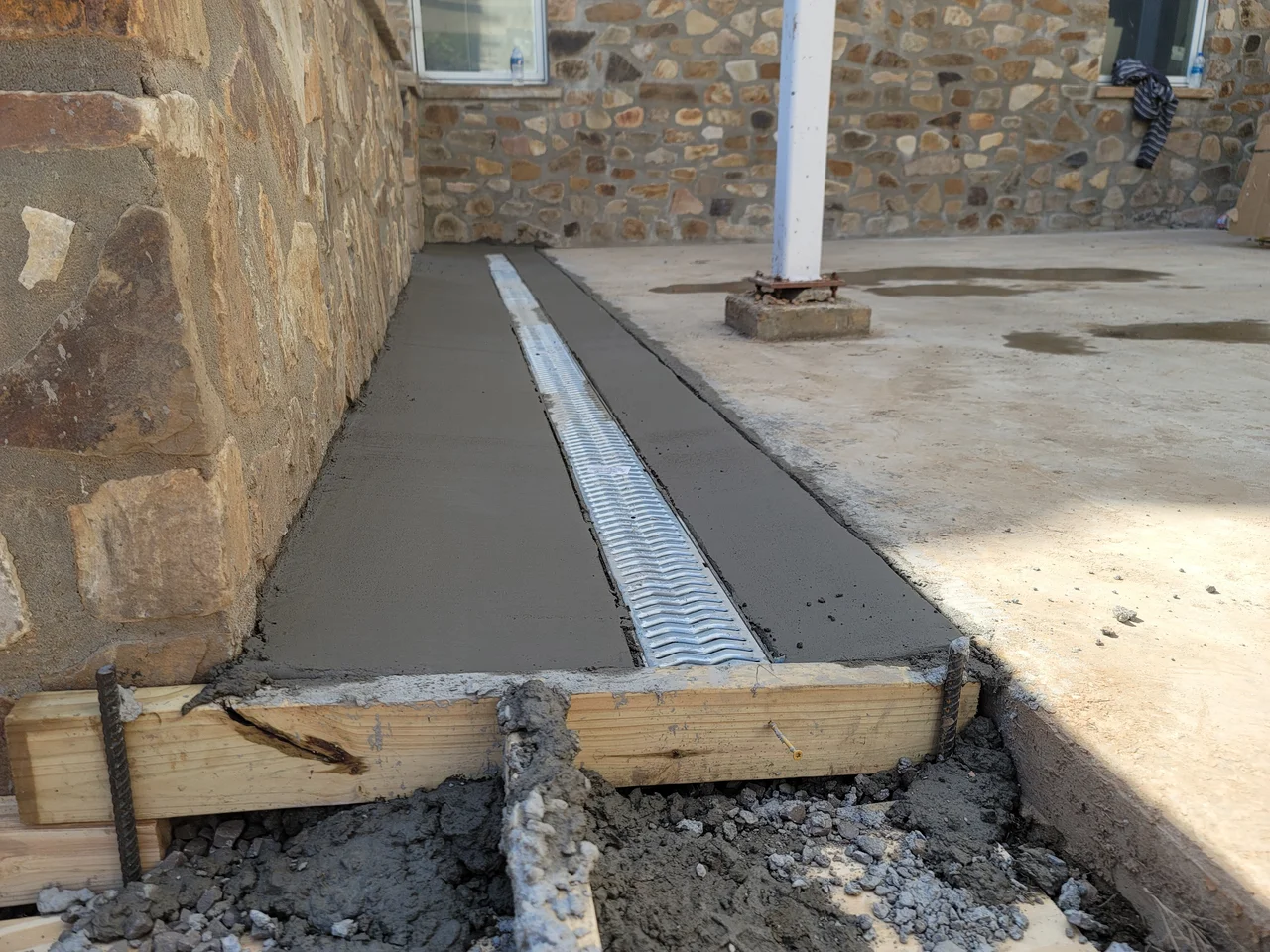 A poured concrete apron with a channel drain set against the stone wall.