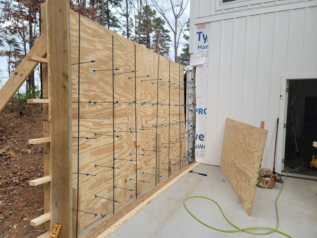 Braced plywood formwork with rebar set against the house wall.
