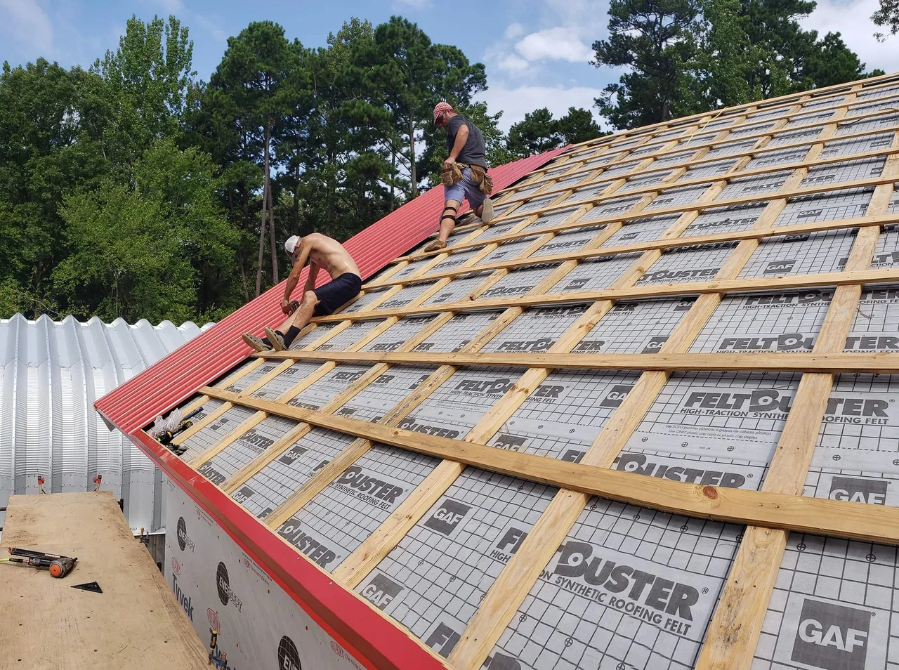 A roofer working across purlins and underlayment on the main roof.