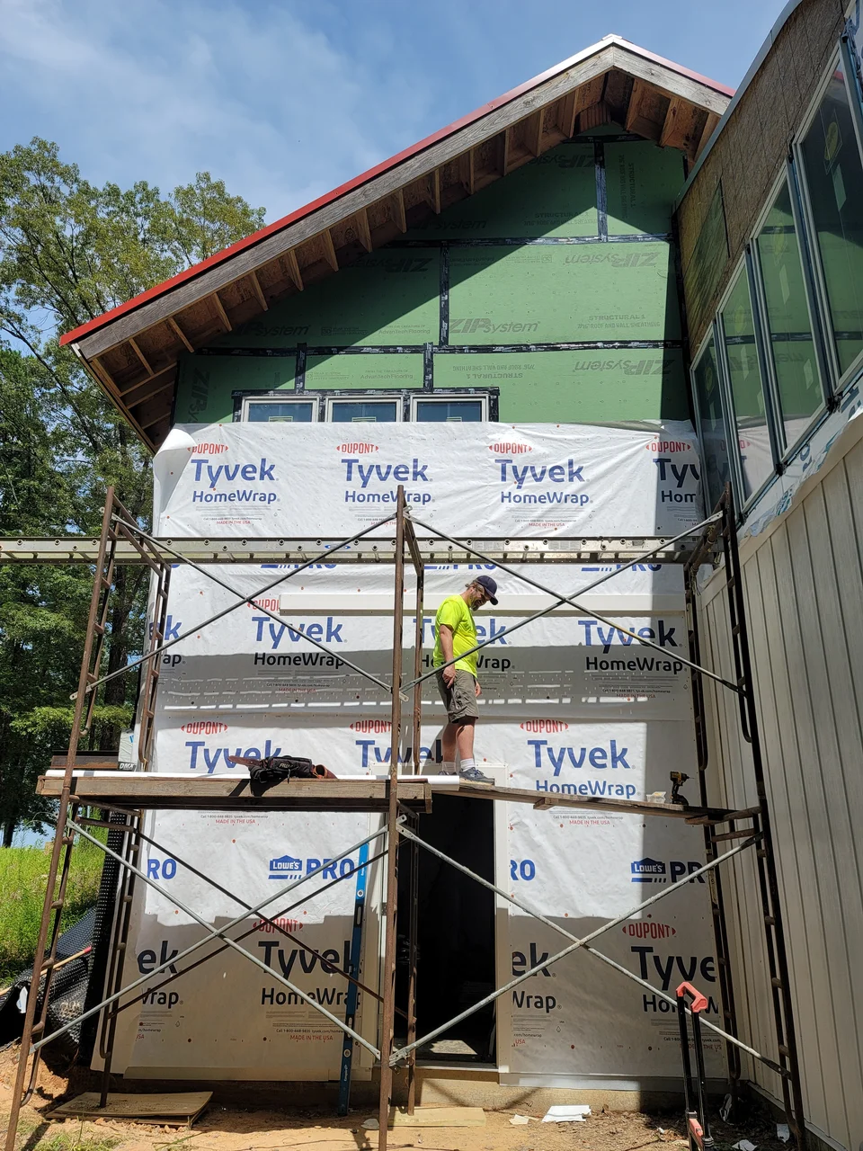 The gable wrapped in housewrap with scaffolding and a worker in place.