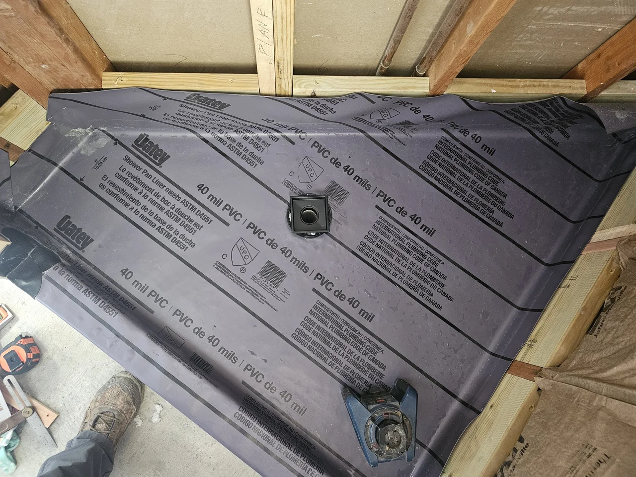 A PVC shower pan liner installed over the subfloor with the drain flange set.