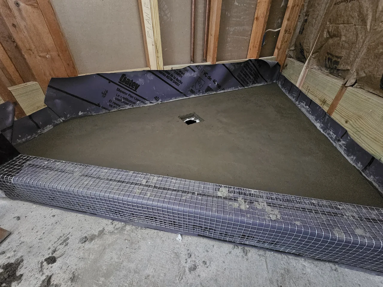A freshly floated mortar mud bed sloped to a centre drain with a lath-reinforced curb.
